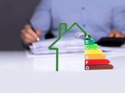 Man sieht ein Haus und eine Grafik der Energieeffizienzklassen vor einem Mann mit einem Ordner