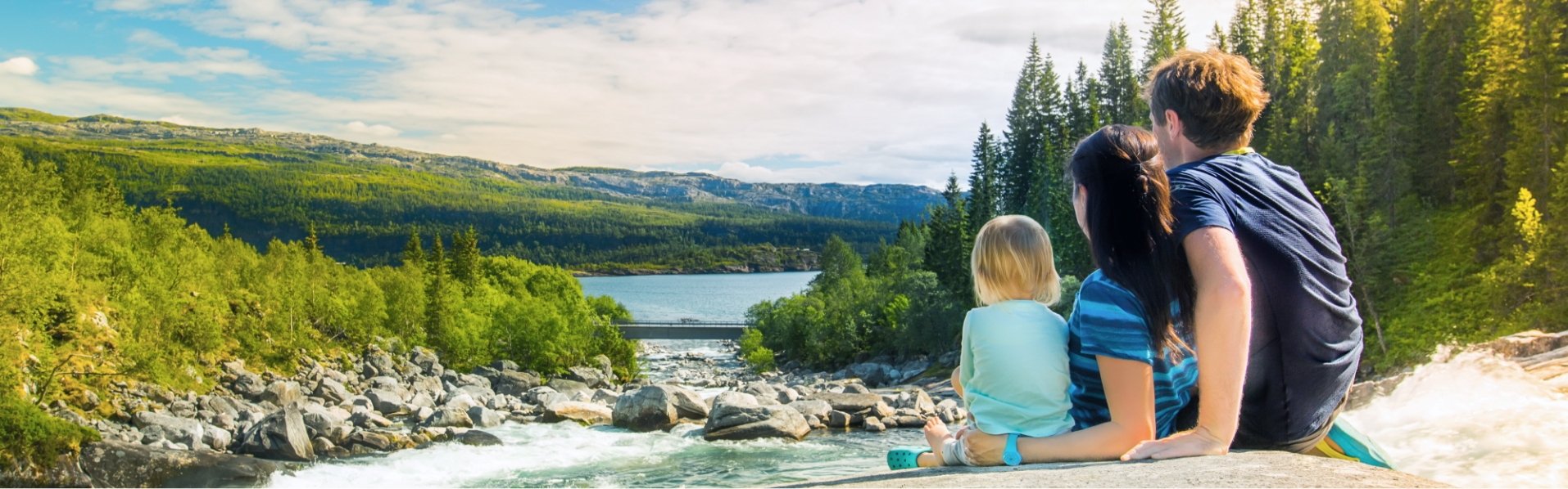 Familie sitzt an einem Fluss mit einem Stausee mit Wasserkraftwerk zur Stromerzeugung im Hintergrund