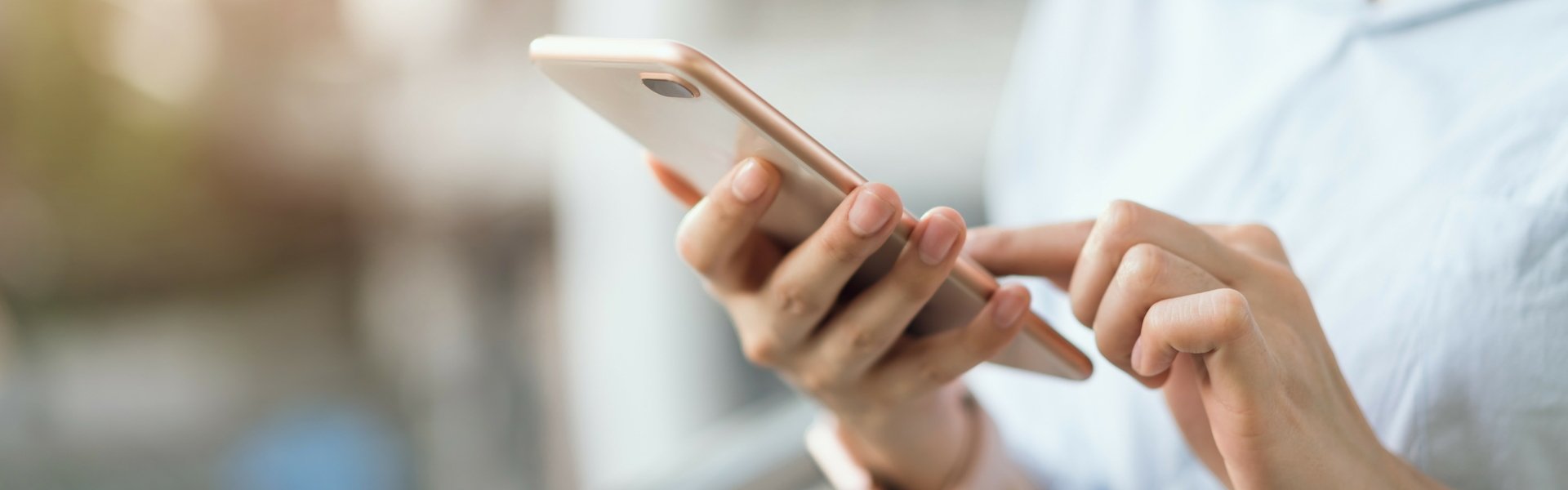 Frau steht vor einem Fenster und gibt etwas auf ihrem Handy ein