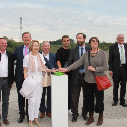 Ministerpräsident Winfried Kretschmann, EnBW-Vorstand Andreas Schell, Mitarbeiter der Erdgas Südwest und Besucher stehen bei der Eröffnung einer weiteren, schwimmende Photovoltaik-Anlage Baden-Württembergs vor dem Rednerpult.