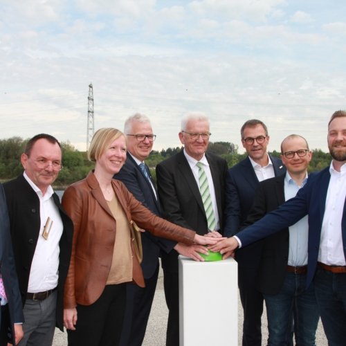 Ministerpräsident Winfried Kretschmann, EnBW-Vorstand Andreas Schell und Mitarbeiter der Erdgas Südwest stehen bei der Eröffnung einer weiteren, schwimmende Photovoltaik-Anlage Baden-Württembergs vor dem Rednerpult.