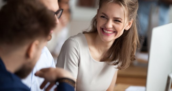 Lächelnde junge Frau im Gespräch mit Kollegen am gemeinsamen Arbeitsplatz