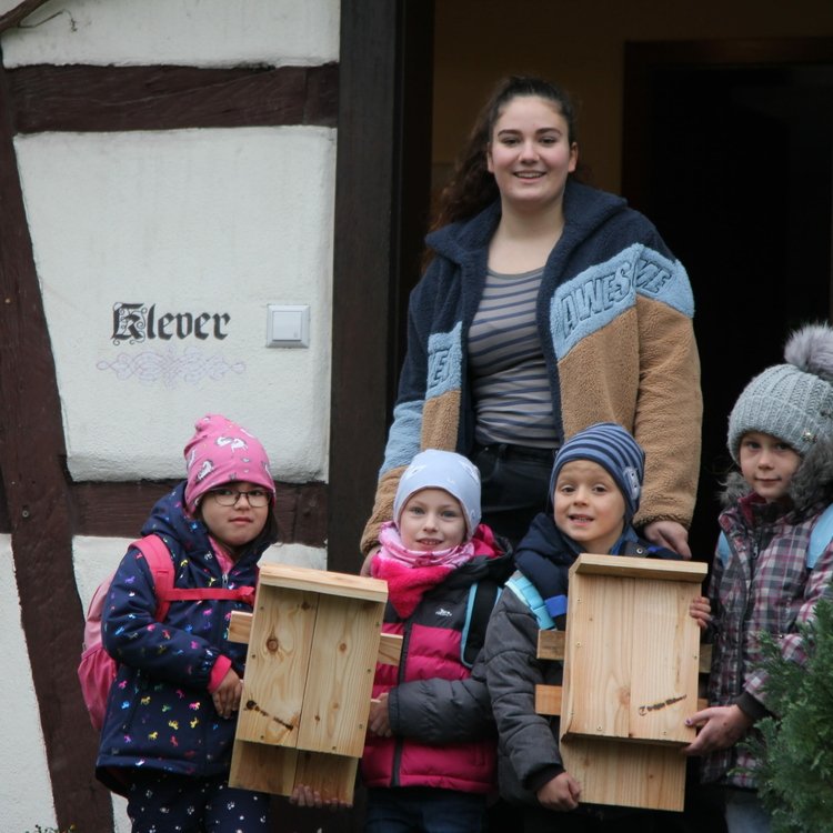 Zu sehen ist eine FÖJ-Mitarbeiterin der Erdgas Südwest mit Kindern, die gerade ihre Nistkasten erfolgreich zusammengebaut haben.