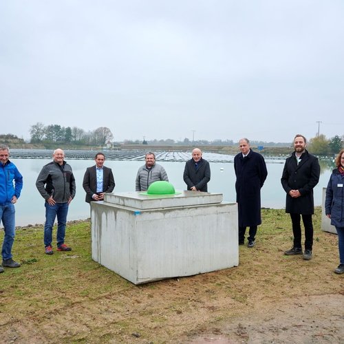 Man sieht ein Gruppenbild vor einer schwimmenden PV Anlage