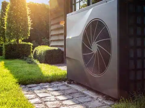 Außengerät einer Wärmepumpe mit Ventilator in einem grünen Garten vor einem Haus